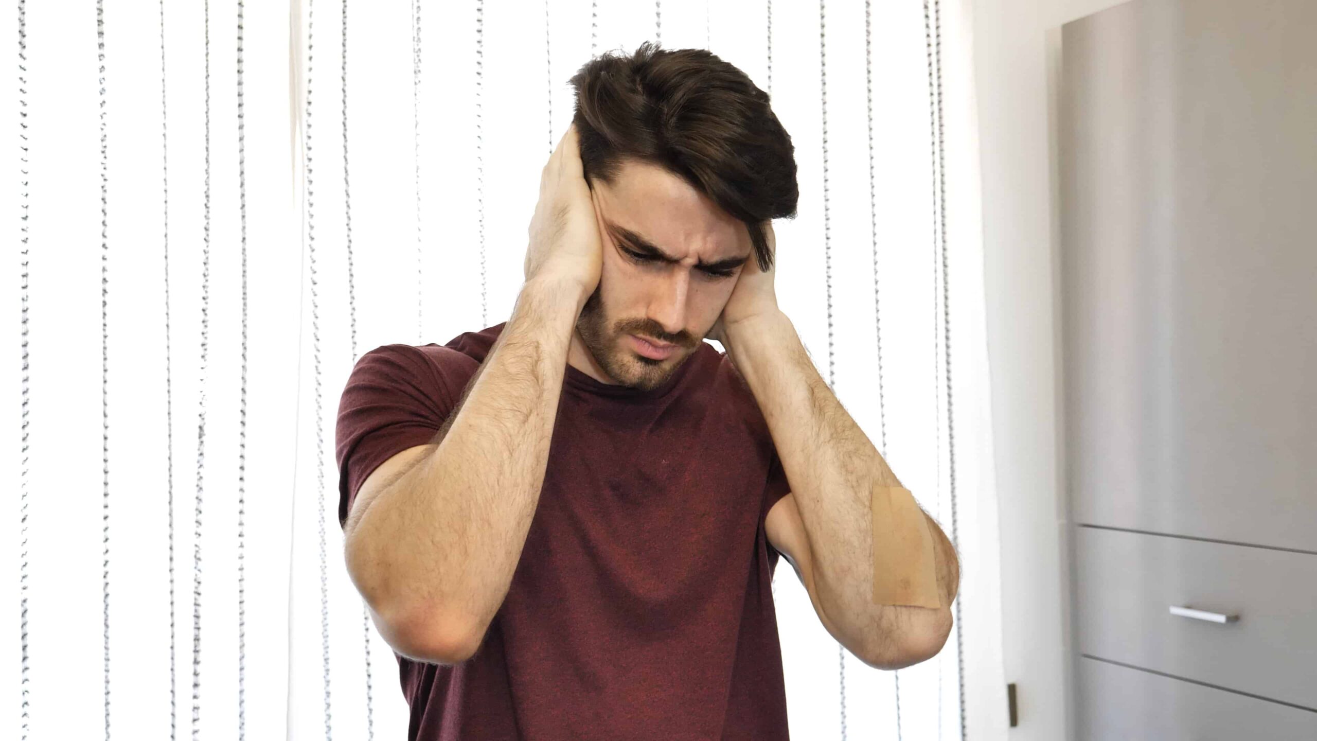 Young man covering his ears, too much noise Handsome young man covering his ears, stressed or unhappy because of too much noise. Indoors shot