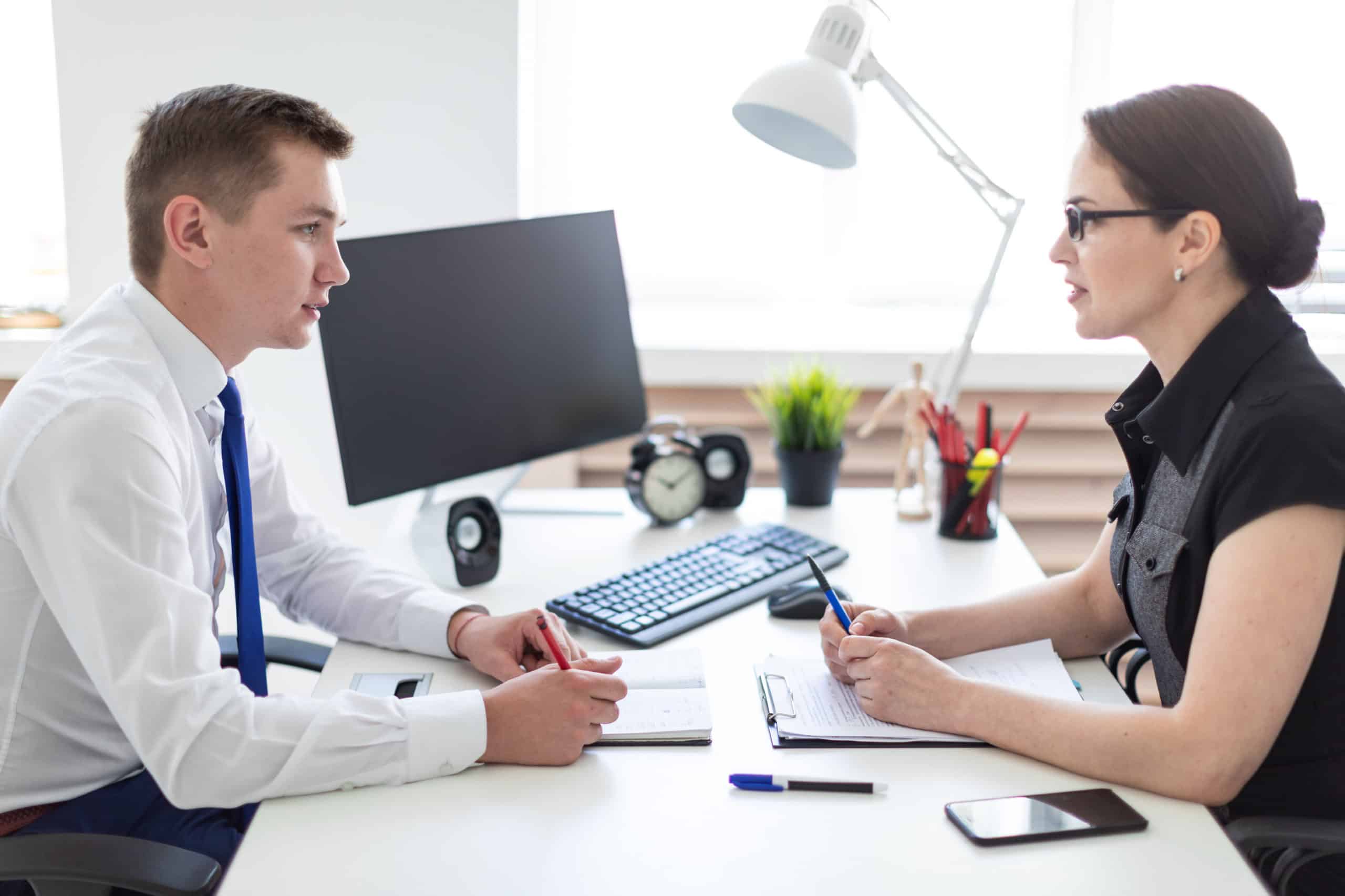 young man and women having a conversation over a desk at work autism and employment, autism workplace accommodation