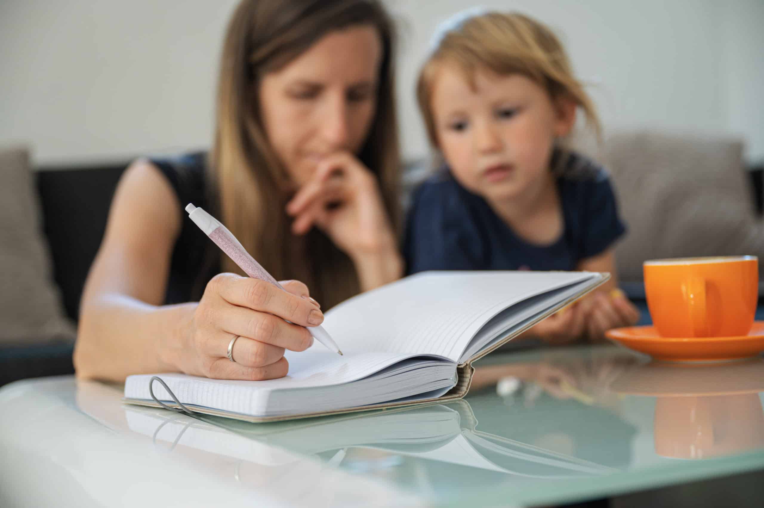 Mother writing in notebook with child autism data tracking, treatment tracking autism